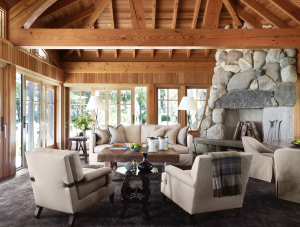 living room chairs with blanket thrown atop. wood vaulted ceilings. rock fireplace, big windows.